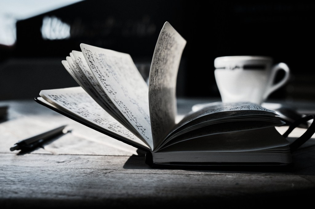 Black and white photo of a pen and coffee mug next to an open journal.