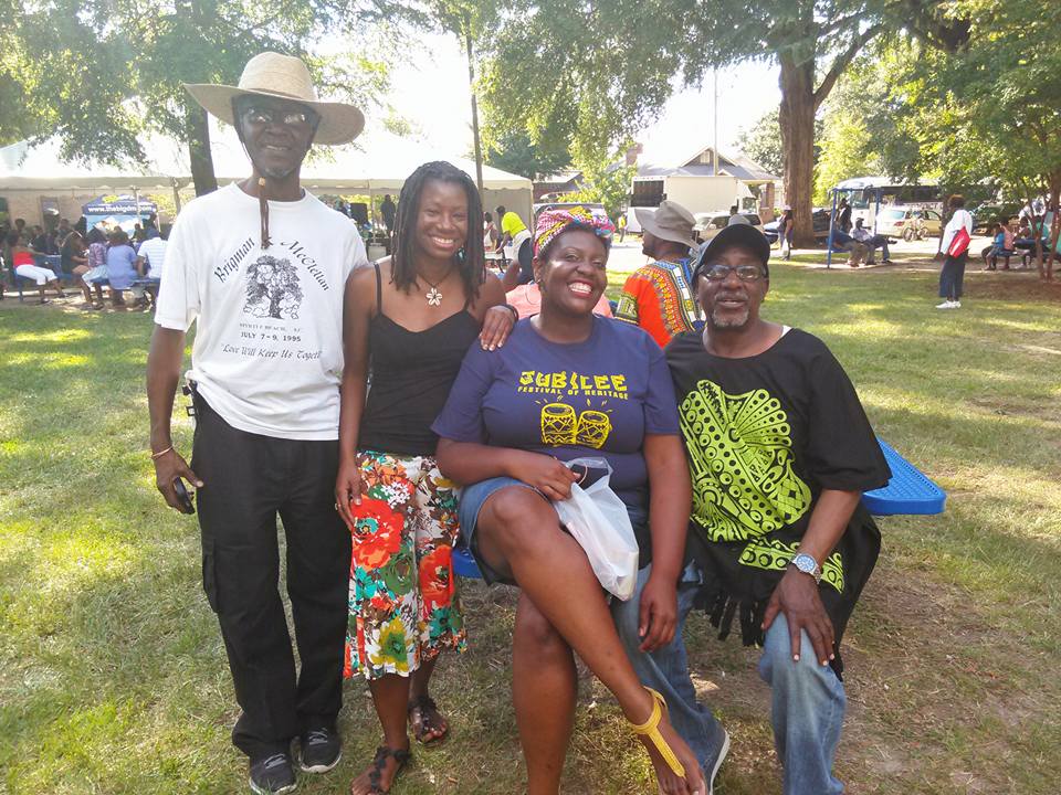 Photo of Dr. Moore in a park, seated, with three people surrounding her. All are smiling at the viewer.