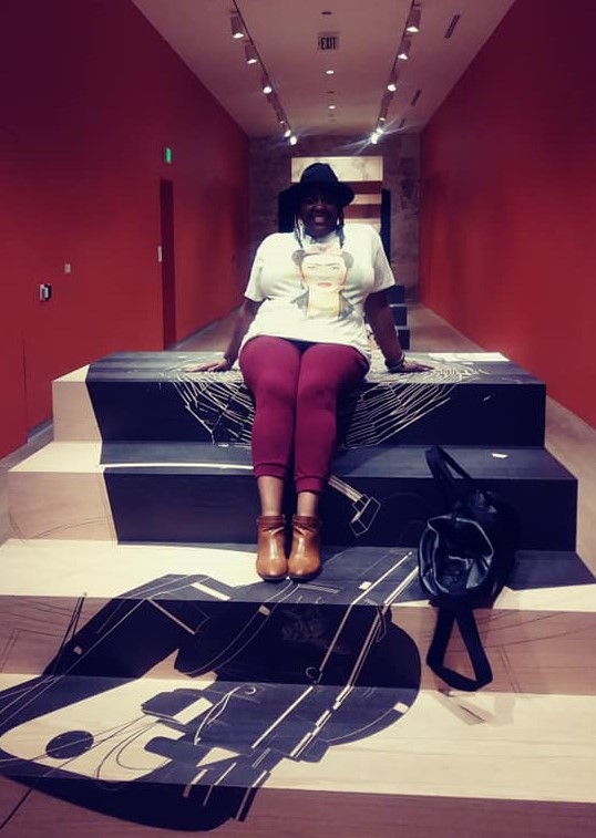 Photo of Dr. Moore sitting on an art installation of a short flight of stairs, decorated in blue designs.