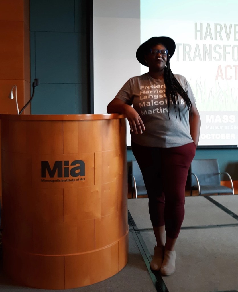 Photo of Dr. Moore leaning on a podium on a stage in front of a screen.